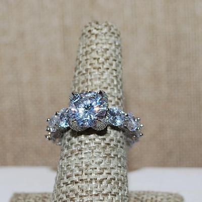 Size 9 Very Interesting Infinity Style Ring with Single Main Stone & FULL Band of Round Clear Stones on a Silver Tone Band (8.9g)