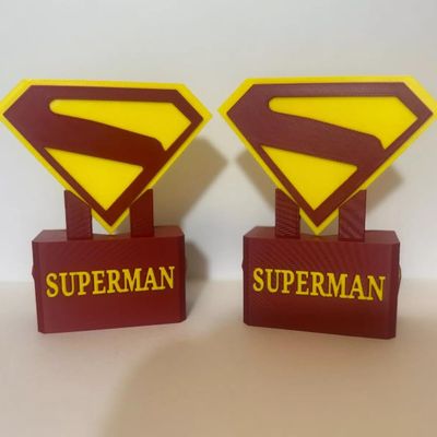 Pair of 3D-printed Superman logo desk displays or bookends in red and yellow plastic.