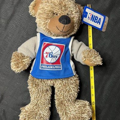 Plush teddy bear wearing a Philadelphia 76ers jersey and grey hoodie, featuring an official NBA tag and measuring approximately 15 inches...