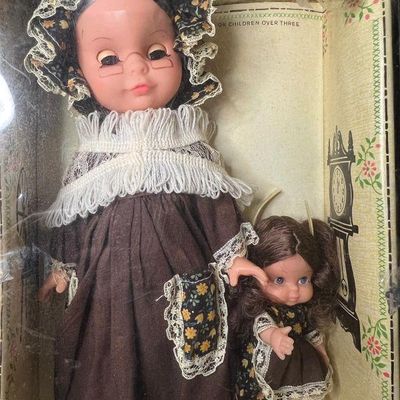 Vintage grandmother and child doll set in original display box, featuring floral bonnet, lace trim, and wire-rim glasses.