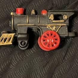 Vintage cast iron toy steam locomotive with black body, gold accents, and red wheels.