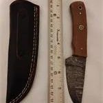 Damascus steel fixed-blade knife with a brown handle, shown alongside its black leather sheath and a wooden ruler for scale.