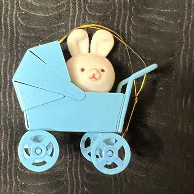 Vintage miniature flocked bunny in a blue plastic baby carriage ornament, featuring a gold hanging string.