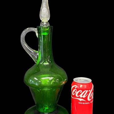 Sale Photo Thumbnail #25: This mid-century hand-blown art glass decanter is believed to be made by the Bischoff Glass Company in the 1950s or 1960s. The color is vibrant emerald green. There is a rough pontil mark on the base, a clear applied handle, and a clear flame-shaped stopp