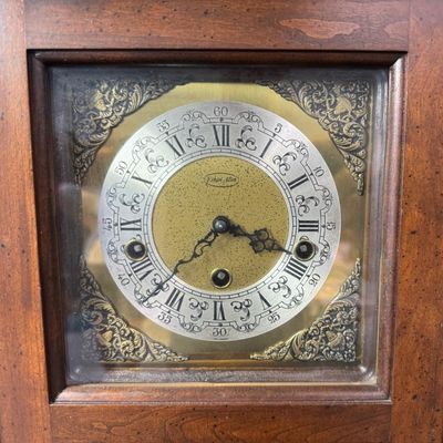 Sale Photo Thumbnail #48: This piece features a fluted wooden case and lower viewing glass showcasing the brass pendulum bob. It was made in West Germany. The key is included. The clock is working at the time of catalog. Measurement: 26.5”H x 12.5”W x 5.5”D. [MI]