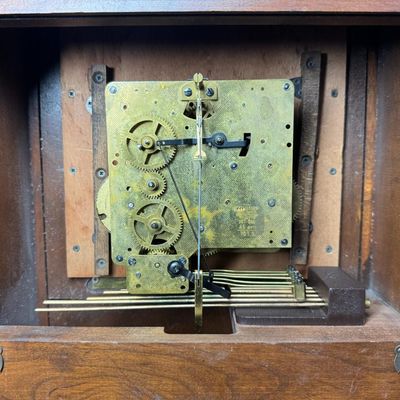 Sale Photo Thumbnail #51: This piece features a fluted wooden case and lower viewing glass showcasing the brass pendulum bob. It was made in West Germany. The key is included. The clock is working at the time of catalog. Measurement: 26.5”H x 12.5”W x 5.5”D. [MI]