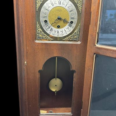 Sale Photo Thumbnail #49: This piece features a fluted wooden case and lower viewing glass showcasing the brass pendulum bob. It was made in West Germany. The key is included. The clock is working at the time of catalog. Measurement: 26.5”H x 12.5”W x 5.5”D. [MI]