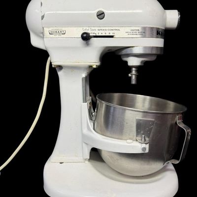 Sale Photo Thumbnail #104: This features all-metal internal gears, and was built during a period when Hobart manufactured KitchenAid appliances. It is complete with a whisk and dough hook. Working at the time of catalog. Measurement: 17” x 13” x 9”. [LG]