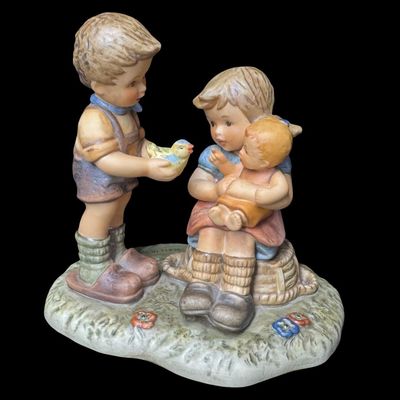 Sale Photo Thumbnail #133: This 1999 piece is numbered BH 80, and was created in Thailand. It depicts a young boy standing and showing a small yellow songbird to a sitting girl who is cradling a doll or baby. Includes the original box. Measurement of figurine: 5.5” x 6”. [AG]