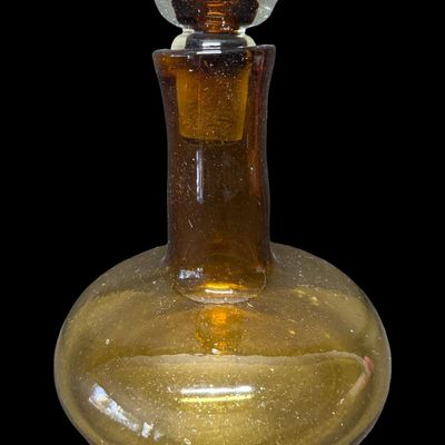 Sale Photo Thumbnail #141: This mid-century hand-blown art glass ship’s decanter is believed to be made by Blenko, or other art glass company of the era. Often referred to as a “Captain’s Decanter,” this piece has a wide, low-gravity base for stability. It is amber in color