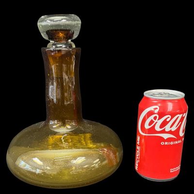 Sale Photo Thumbnail #144: This mid-century hand-blown art glass ship’s decanter is believed to be made by Blenko, or other art glass company of the era. Often referred to as a “Captain’s Decanter,” this piece has a wide, low-gravity base for stability. It is amber in color