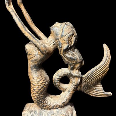 Sale Photo Thumbnail #569: This piece features a cast mermaid with outstretched arms on a heavy base. There is minimal surface rust. Measurement: 9” x 6.5”. [AG]