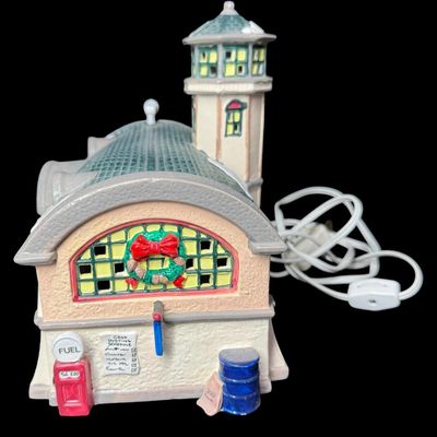 Sale Photo Thumbnail #642: This retired piece features a hand painted ceramic lighted building styled as an airfield hangar, attached control tower, and an integrated single engine prop plane inside. There are no obvious chips or cracks. Measurement: 11” x 8.25”. [AG]