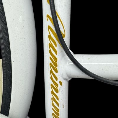 Sale Photo Thumbnail #649: This is constructed of a lightweight aluminum step-through frame, with distinct gold script accents. It features front and rear hand-operated side pull caliper brakes. It is gently used, though there may be stains or pitting in places. [AG]
