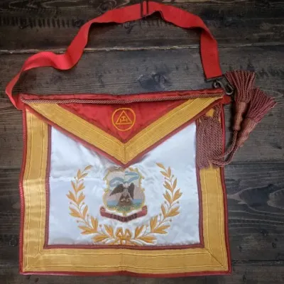 Sale Photo Thumbnail #235: A striking Masonic Royal Arch Past High Priest apron, rich in symbolism and finely detailed with gold bullion embroidery on satin.

Royal Arch Symbolism: The apron includes the characteristic red border and the emblem of the Royal Arch
Embroidered Detail:
