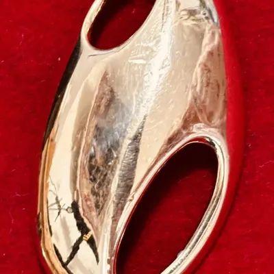 Sale Photo Thumbnail #119: This is a rare Trifari brooch from the 1970s designed by Kunio Matsumoto. It features a modernist abstract design in gold tone, measuring 2.5 inches in length. Signed by Trifari, this vintage piece is oval in shape and does not contain any stones. It is a