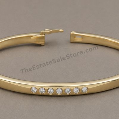 Sale Photo Thumbnail #30: Polished yellow-gold hinged bangle bracelet accented across the front with seven round diamond-style stones in flush settings. Features a box clasp with safety catch. Interior circumference approximately 7 inches; marked 14K; estimated gross weight 11.9 g
