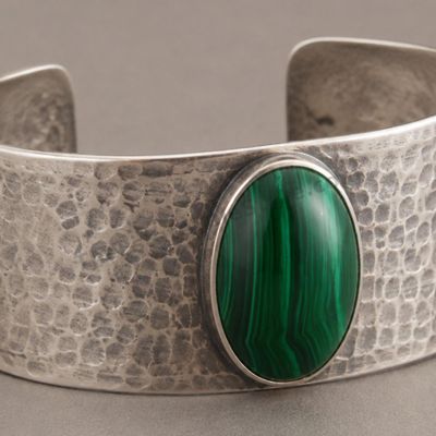 Sale Photo Thumbnail #32: Wide open-back sterling silver cuff with hand-hammered texture and a central oval malachite-style cabochon showing vivid green banding. Approximate interior circumference 6.5 inches with a 1.25-inch opening; estimated gross weight 42.3 grams. Marked 925. 