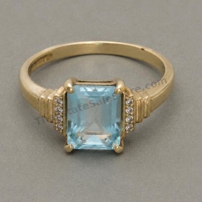 Sale Photo Thumbnail #66: Yellow-gold ring set with a large rectangular sky-blue topaz-style stone flanked by small clear accent stones. Marked 10K; approximate ring size 8 and estimated gross weight 5.7 grams. Moderate scratches are present on the band, with light abrasions to th