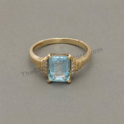 Sale Photo Thumbnail #65: Yellow-gold ring set with a large rectangular sky-blue topaz-style stone flanked by small clear accent stones. Marked 10K; approximate ring size 8 and estimated gross weight 5.7 grams. Moderate scratches are present on the band, with light abrasions to th