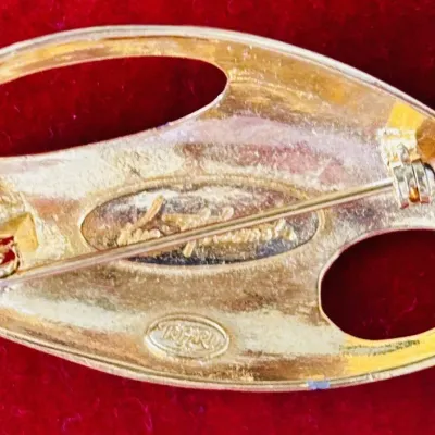 Sale Photo Thumbnail #147: This is a rare Trifari brooch from the 1970s designed by Kunio Matsumoto. It features a modernist abstract design in gold tone, measuring 2.5 inches in length. Signed by Trifari, this vintage piece is oval in shape and does not contain any stones. It is a
