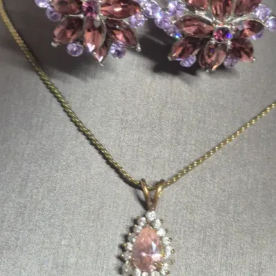 Sale Photo Thumbnail #204: Beautiful 1.5 carat Amethyst gold tone Necklace & Amethyst Rhinestone Earrings
> herringbone chain necklace....12"long
> Amethyst pendant .75" dangle
> Amethyst earring are clip style.