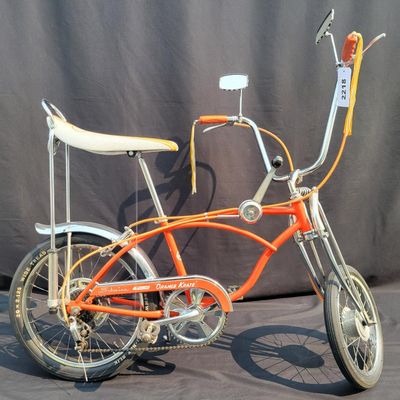 Sale Photo Thumbnail #2: Schwinn Sting-Ray Orange Krate with 5-speed Stik-Shift, springer front fork, high-rise handlebars, orange glitter grips, tall sissy bar, 1990's reproduction schwinn krate banana seat, original white letter slik rear tire, rear reflector, a PAIR of Schwinn