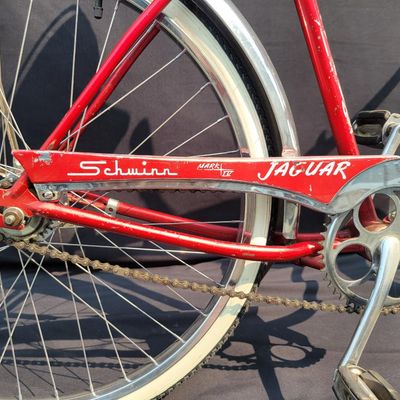 Sale Photo Thumbnail #112: Red Schwinn Jaguar with whitewall tires, full fenders, rear carrier, tank-style frame insert, red Mesinger-style saddle, bell, front light equipment and Jaguar-marked chainguard. The rear wheel sports a Bendix Red Band 2 speed Automatic Hub.  A nicely equ