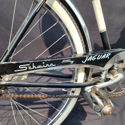 Sale Photo Thumbnail #123: Black Schwinn Jaguar with whitewall tires, full fenders, rear carrier, tank insert, front headlight, rear mud flap and black/white saddle. Attractive survivor with a largely period-correct look and good completeness. Shows scuffs, oxidation and general vi