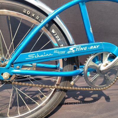 Sale Photo Thumbnail #142: Blue Schwinn Deluxe Sting-Ray single speed coaster brake bicycle with blue banana seat, tall sissy bar, blue grips, high-rise handlebars, fenders and rear reflector. Very complete, original paint and attractive with moderate vintage wear to the saddle, gr