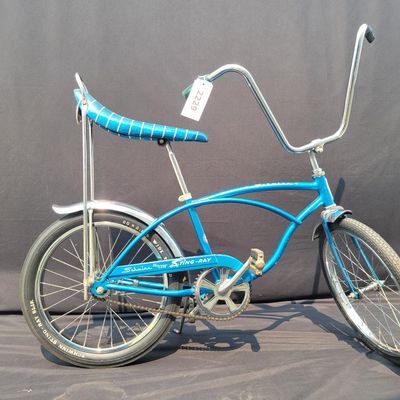 Sale Photo Thumbnail #141: Blue Schwinn Deluxe Sting-Ray single speed coaster brake bicycle with blue banana seat, tall sissy bar, blue grips, high-rise handlebars, fenders and rear reflector. Very complete, original paint and attractive with moderate vintage wear to the saddle, gr