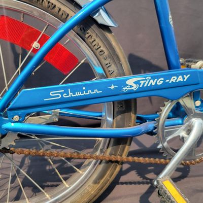 Sale Photo Thumbnail #168: Blue Schwinn Sting-Ray with banana saddle, tall sissy bar, high-rise handlebars, blue grips, chrome rear fender/reflector. Classic muscle-bike styling in good vintage condition with expected wear to the seat, grips, paint and chrome. Major components are 