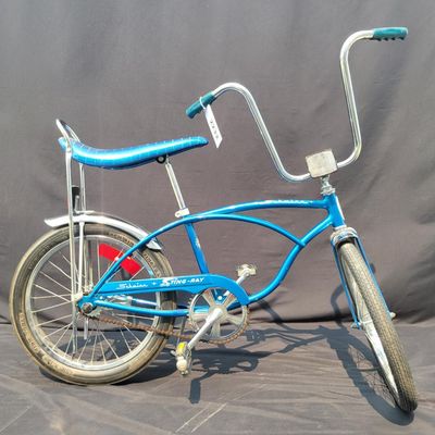 Sale Photo Thumbnail #167: Blue Schwinn Sting-Ray with banana saddle, tall sissy bar, high-rise handlebars, blue grips, chrome rear fender/reflector. Classic muscle-bike styling in good vintage condition with expected wear to the seat, grips, paint and chrome. Major components are 
