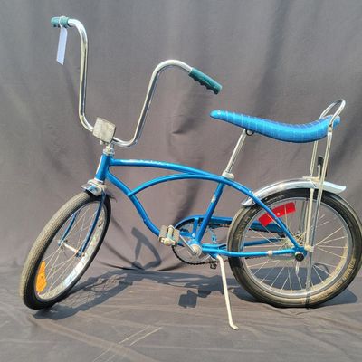 Sale Photo Thumbnail #174: Blue Schwinn Sting-Ray with banana saddle, tall sissy bar, high-rise handlebars, blue grips, chrome rear fender/reflector. Classic muscle-bike styling in good vintage condition with expected wear to the seat, grips, paint and chrome. Major components are 