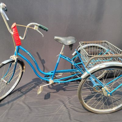 Sale Photo Thumbnail #208: Blue Schwinn Town & Country adult tricycle with step-through frame, large rear wire cargo basket, Town & Country chainguard, fenders, reflectors and black replacement saddle. Complete and useful vintage trike showing surface rust, basket corrosion, drivet