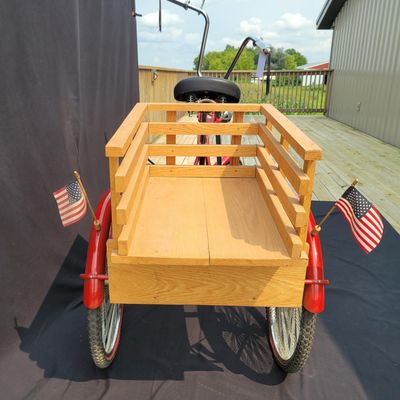 Sale Photo Thumbnail #214: Custom red 3-speed cargo tricycle with long wood-slatted rear cargo bed, tall handlebars, flame-style saddle, headlight, flags and assorted bottle/cargo accessories. Chainguard is marked “Ray Spoiler / 3 Speed.” A fun one-off custom build with strong 