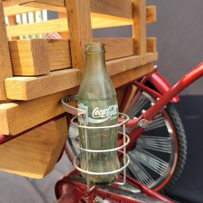 Sale Photo Thumbnail #211: Custom red 3-speed cargo tricycle with long wood-slatted rear cargo bed, tall handlebars, flame-style saddle, headlight, flags and assorted bottle/cargo accessories. Chainguard is marked “Ray Spoiler / 3 Speed.” A fun one-off custom build with strong 