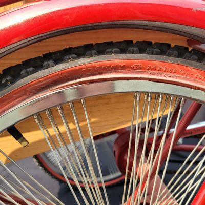 Sale Photo Thumbnail #213: Custom red 3-speed cargo tricycle with long wood-slatted rear cargo bed, tall handlebars, flame-style saddle, headlight, flags and assorted bottle/cargo accessories. Chainguard is marked “Ray Spoiler / 3 Speed.” A fun one-off custom build with strong 