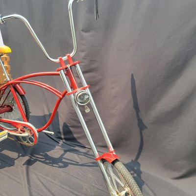 Sale Photo Thumbnail #215: Custom red 3-speed cargo tricycle with long wood-slatted rear cargo bed, tall handlebars, flame-style saddle, headlight, flags and assorted bottle/cargo accessories. Chainguard is marked “Ray Spoiler / 3 Speed.” A fun one-off custom build with strong 