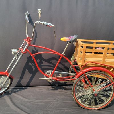 Sale Photo Thumbnail #219: Custom red 3-speed cargo tricycle with long wood-slatted rear cargo bed, tall handlebars, flame-style saddle, headlight, flags and assorted bottle/cargo accessories. Chainguard is marked “Ray Spoiler / 3 Speed.” A fun one-off custom build with strong 