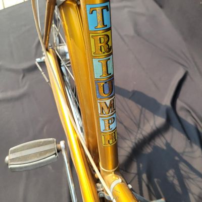 Sale Photo Thumbnail #305: Orange/gold Triumph women's step-through bicycle with full fenders, chainguard, white grips, kickstand and black Specialized replacement saddle. Attractive vintage utility bike with normal paint wear and age. One tire is visibly aged/cracked or low and wi