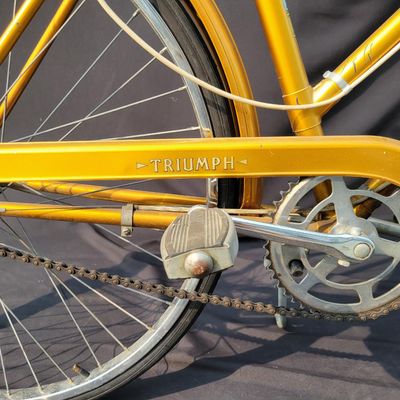 Sale Photo Thumbnail #304: Orange/gold Triumph women's step-through bicycle with full fenders, chainguard, white grips, kickstand and black Specialized replacement saddle. Attractive vintage utility bike with normal paint wear and age. One tire is visibly aged/cracked or low and wi