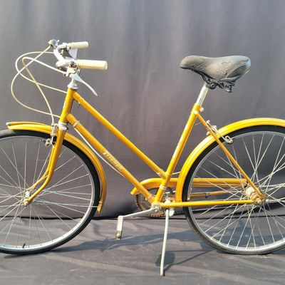 Sale Photo Thumbnail #310: Orange/gold Triumph women's step-through bicycle with full fenders, chainguard, white grips, kickstand and black Specialized replacement saddle. Attractive vintage utility bike with normal paint wear and age. One tire is visibly aged/cracked or low and wi