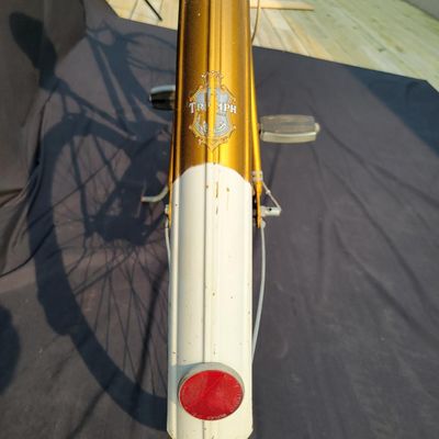Sale Photo Thumbnail #307: Orange/gold Triumph women's step-through bicycle with full fenders, chainguard, white grips, kickstand and black Specialized replacement saddle. Attractive vintage utility bike with normal paint wear and age. One tire is visibly aged/cracked or low and wi
