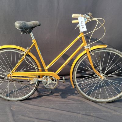 Sale Photo Thumbnail #303: Orange/gold Triumph women's step-through bicycle with full fenders, chainguard, white grips, kickstand and black Specialized replacement saddle. Attractive vintage utility bike with normal paint wear and age. One tire is visibly aged/cracked or low and wi