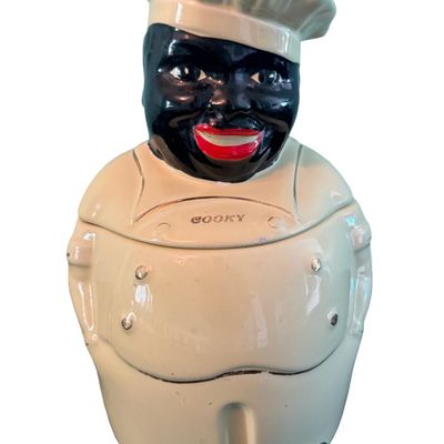 Sale Photo Thumbnail #314: This glazed ceramic cookie jar was produced int the 1940s by the Peal China Company of East Liverpool, Ohio, as part of a historical Black Americana kitchenware line. It features 22K gold accents. There is age related wear, including some fading of the go