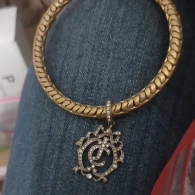 Sale Photo Thumbnail #32: The gold tone juicy bracelet with a JC round charm pendant is a stylish fashion jewelry piece for those who enjoy a statement necklace. The round pendant charm adds a unique touch to the design, complemented by the gold and silver color scheme. The metal 