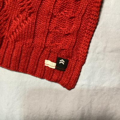 Sale Photo Thumbnail #2: Red cable knit scarf featuring textured diamond and braid knit patterns. Includes a small woven brand tag near the edge. In good pre-owned condition with no visible stains or tears.