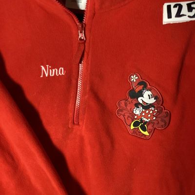 Sale Photo Thumbnail #4: NWT (New with tags) red fleece quarter-zip pullover from The Disney Store, featuring embroidered Minnie Mouse patch on the left chest and embroidered 'Nina' name detail on the right chest. 100% polyester fleece construction. Brand tags attached. Size: Lad
