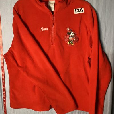 Sale Photo Thumbnail #3: NWT (New with tags) red fleece quarter-zip pullover from The Disney Store, featuring embroidered Minnie Mouse patch on the left chest and embroidered 'Nina' name detail on the right chest. 100% polyester fleece construction. Brand tags attached. Size: Lad